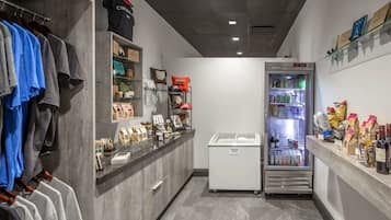 A compact hotel room with a kitchenette, a refrigerator stocked with beverages, and a clothing rack with casual wear.