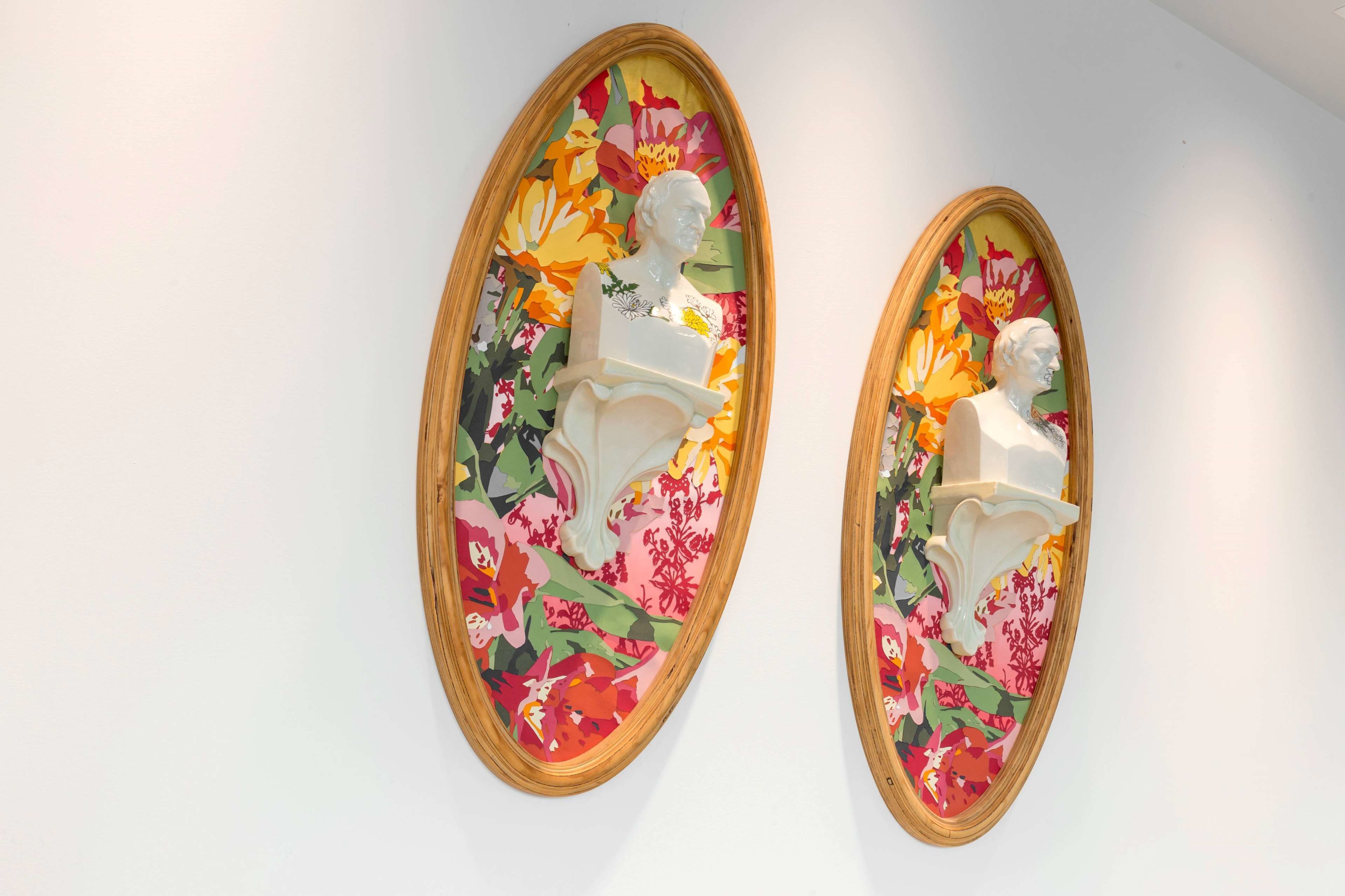 Two white bust sculptures mounted on a wall with a colorful floral pattern.