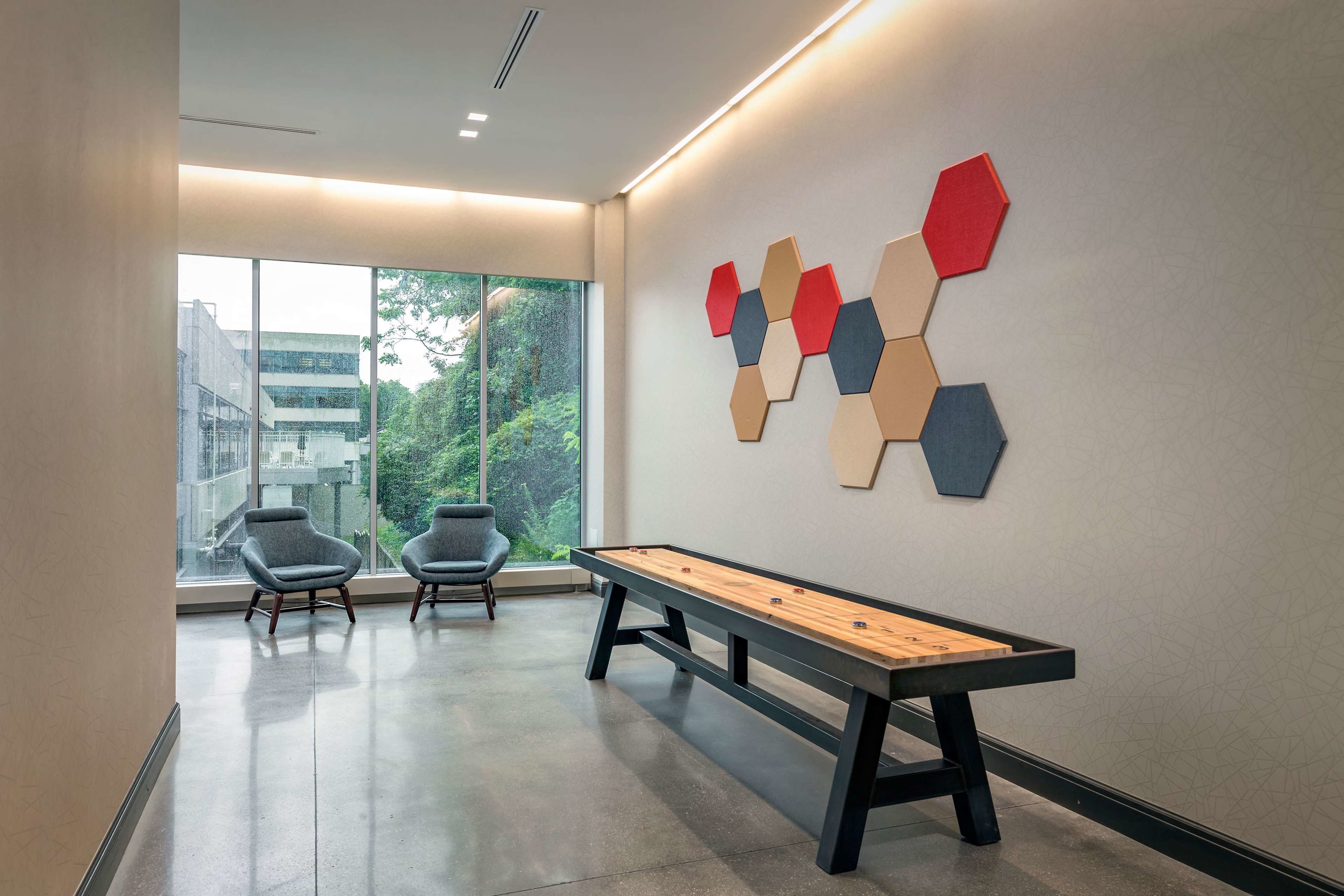 Ein modernes Interieur mit einer langen Holzbank, zwei grauen Stühlen und einem sechseckigen Kunstwerk an der Wand.