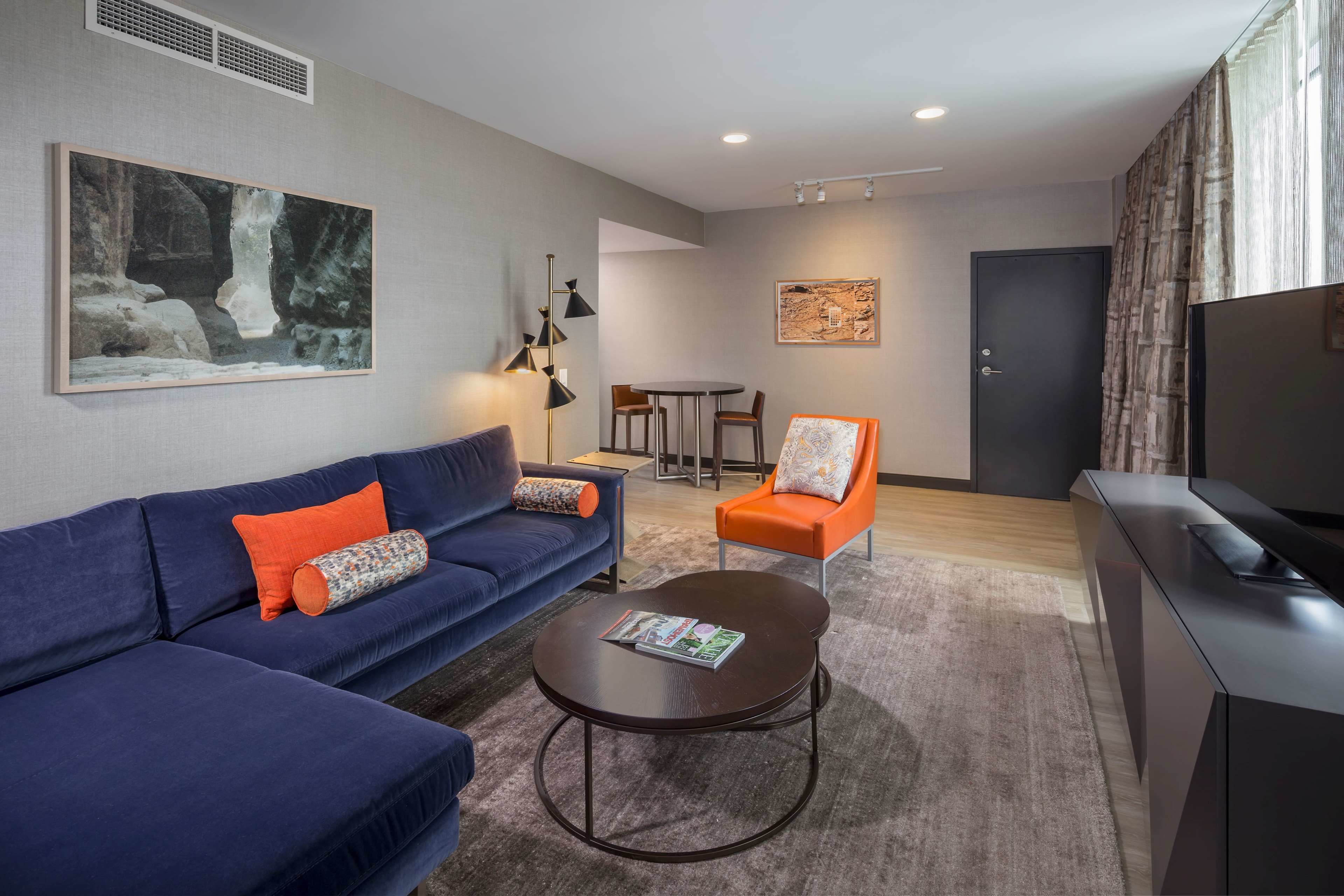Uma sala de estar moderna com um sofá azul, uma poltrona laranja e uma mesa de centro redonda.