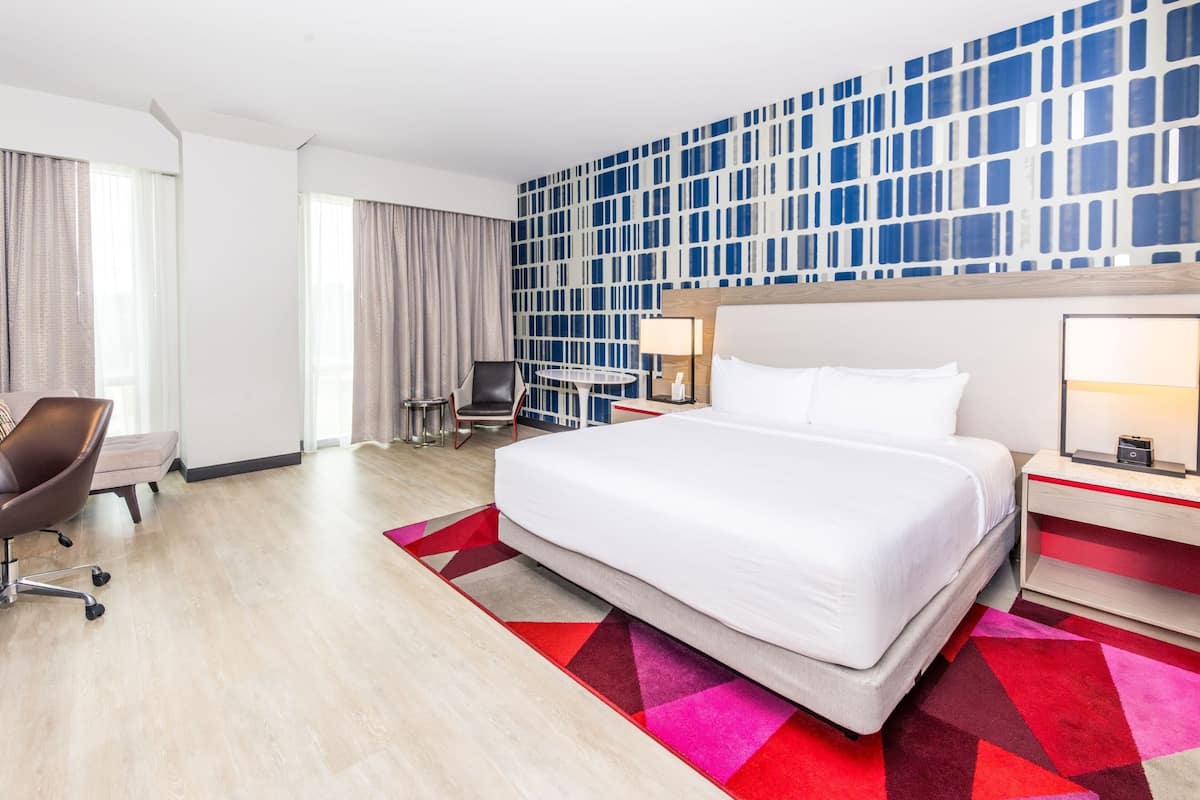 Habitación de hotel con una cama grande, un escritorio, una silla, un televisor y un papel tapiz estampado.