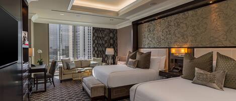 A hotel room with two beds, a desk, a chair, and a view of the city.
