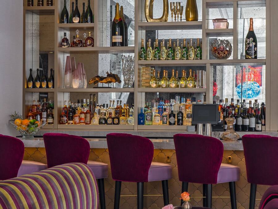 Eine Bar mit mehreren Flaschenregalen, einer Theke und Sitzgelegenheiten mit Samtstühlen.