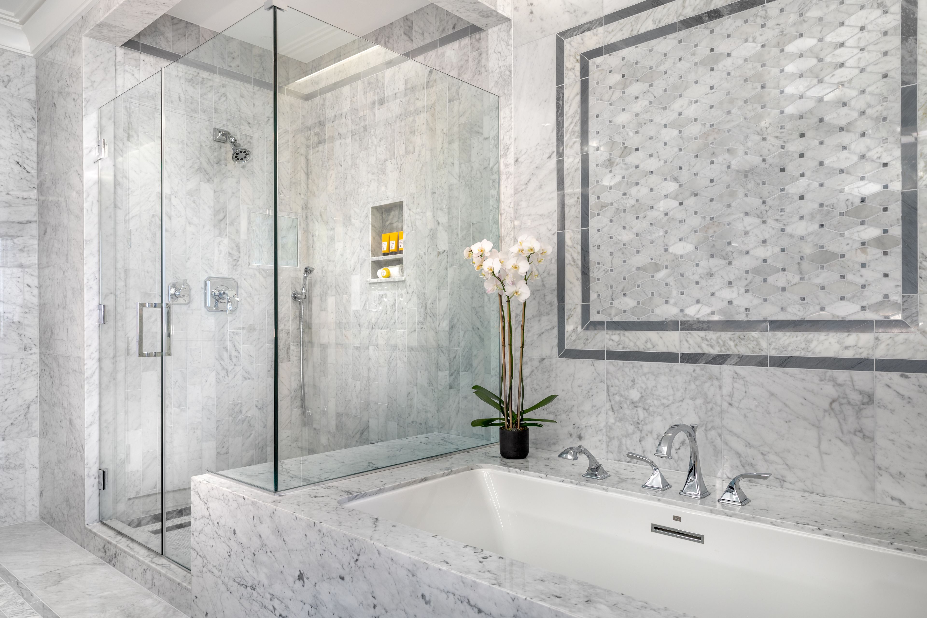 Un baño moderno con ducha envuelta en vidrio, lavamanos de mármol y un patrón decorativo en las baldosas de la pared.