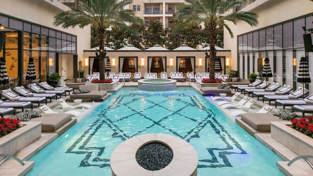 A pool area with lounge chairs and palm trees, surrounded by a building with large windows. - The Post Oak Hotel at Uptown Houston (Houston)