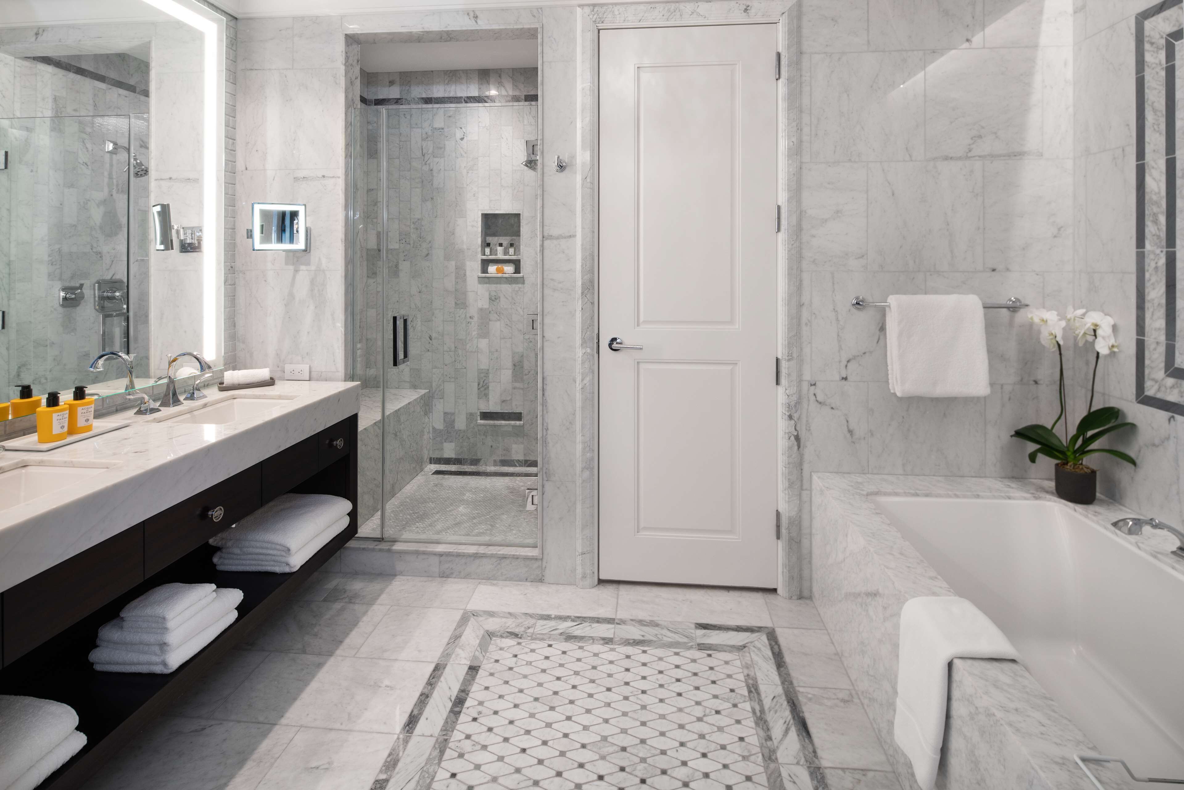 A modern bathroom with a large mirror, dual sinks, a walk-in shower, and a bathtub.