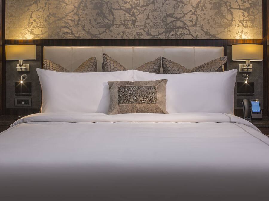 A hotel room with a large bed, a headboard with a patterned design, two bedside lamps, and a control panel on the nightstand.