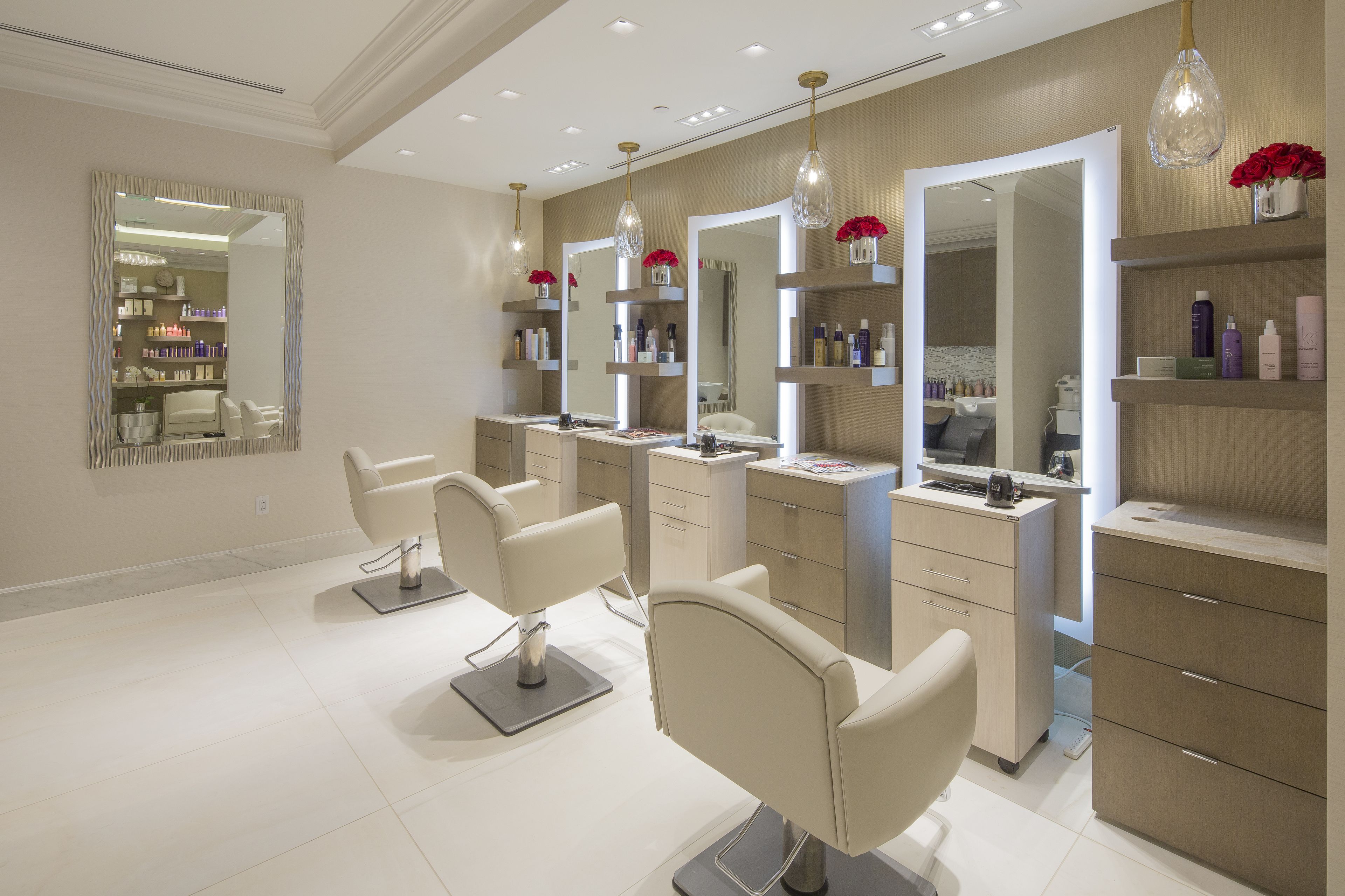 Un moderno salón con tres sillones de peluquería, espejos grandes y estanterías con productos capilares.