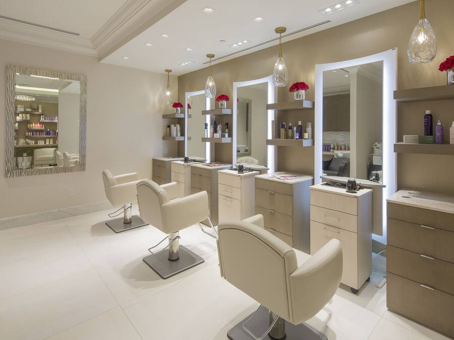 Un moderno salón con tres sillones de peluquería, espejos grandes y estanterías con productos capilares.