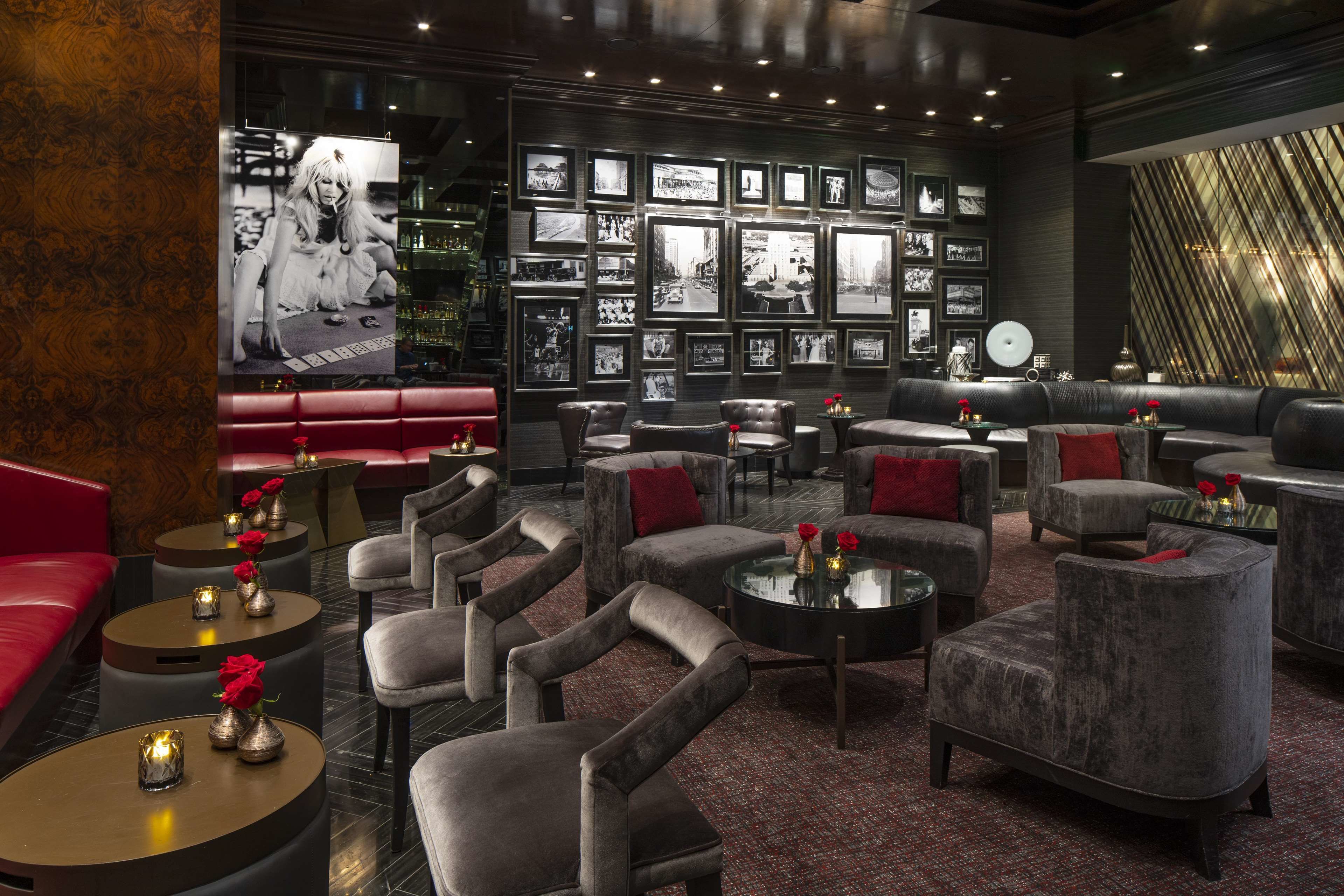 A modern lounge area with leather sofas, armchairs, and round tables, featuring a wall of black-and-white photographs and a large TV screen.