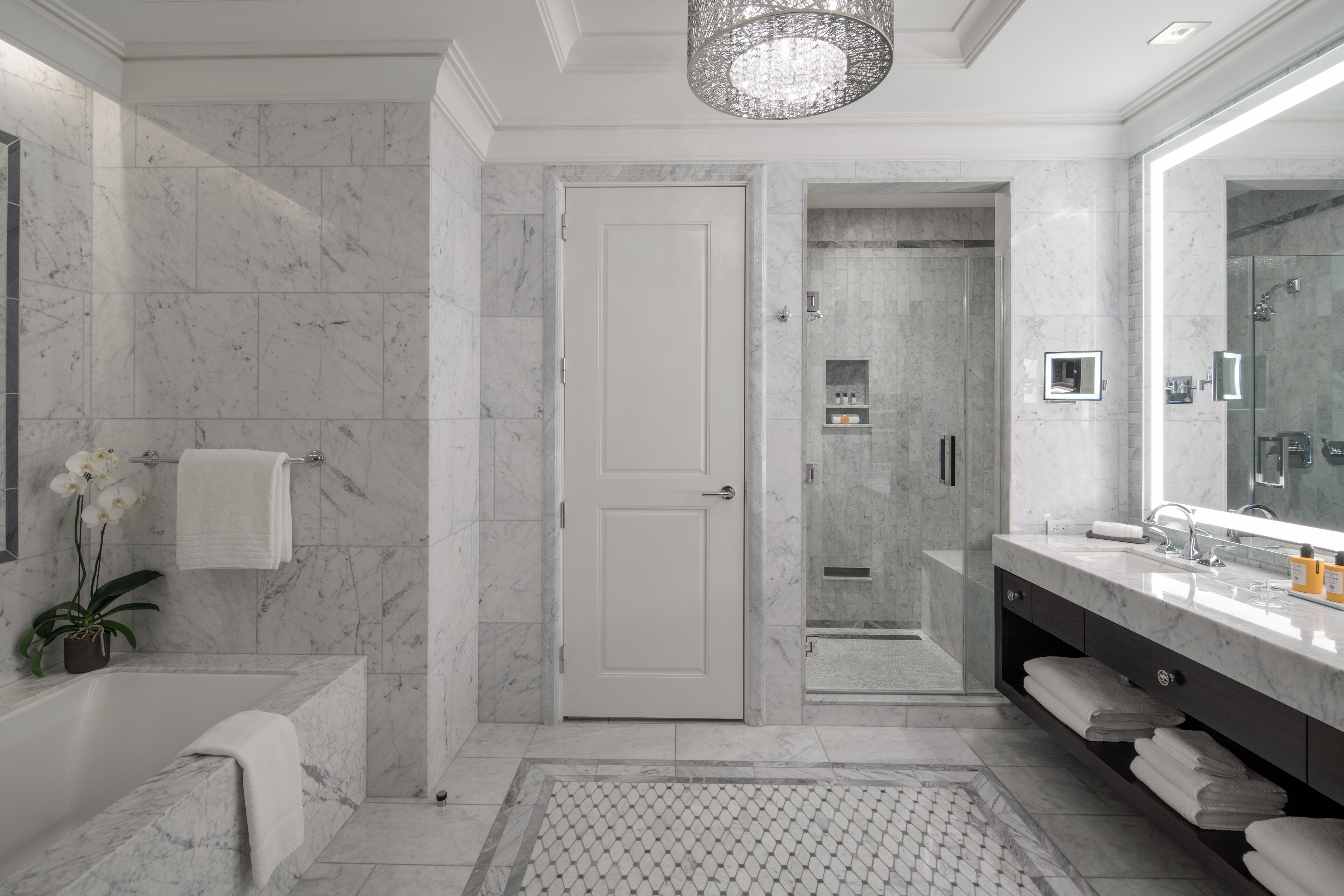 A modern bathroom with a marble floor, a large mirror, a bathtub, and a walk-in shower.