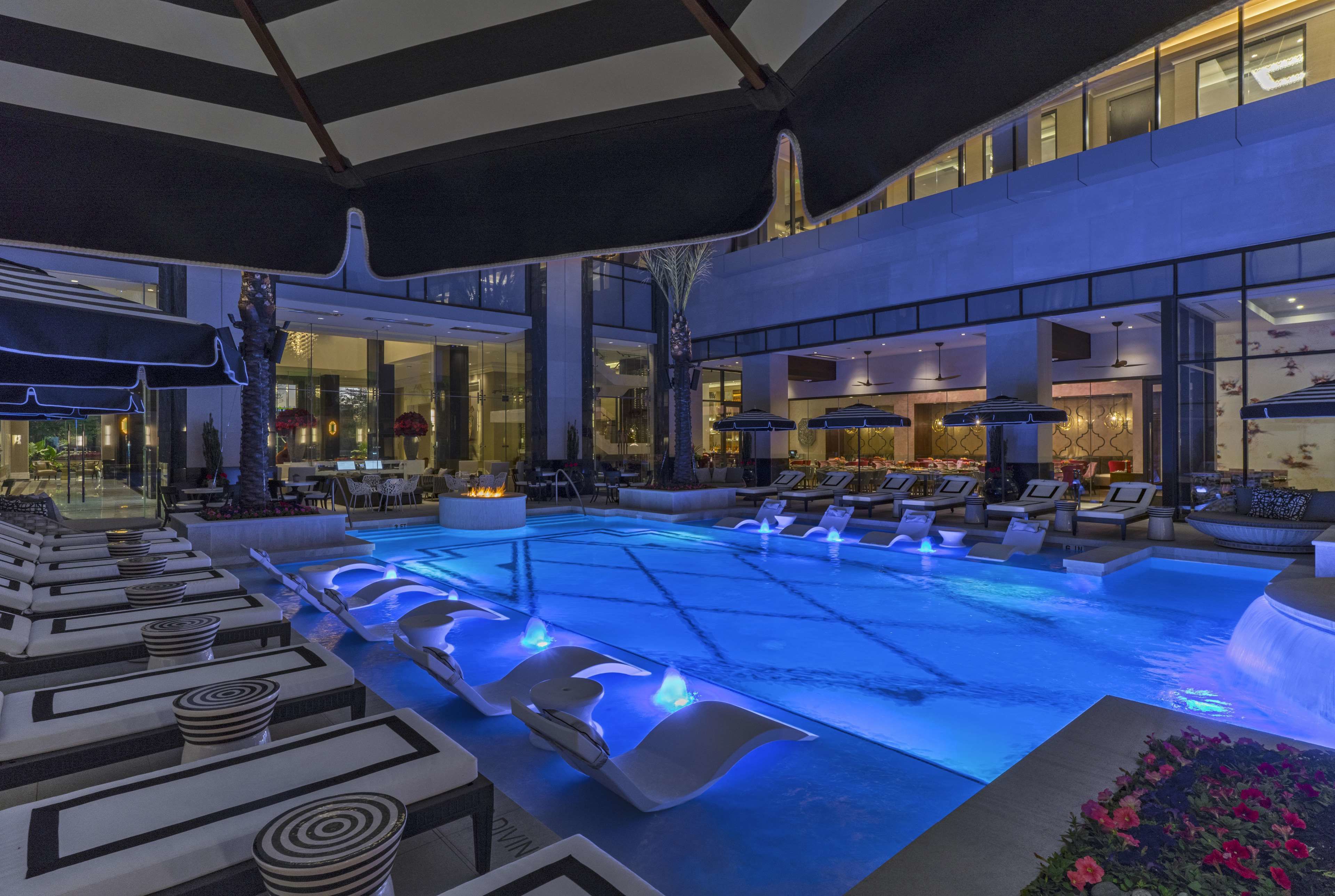 Un área de piscina interior moderna con sillones de descanso, una fuente de agua y un comedor.