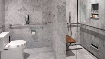 A modern bathroom with a marble floor, a glass shower enclosure, a wooden bench, and a toilet.
