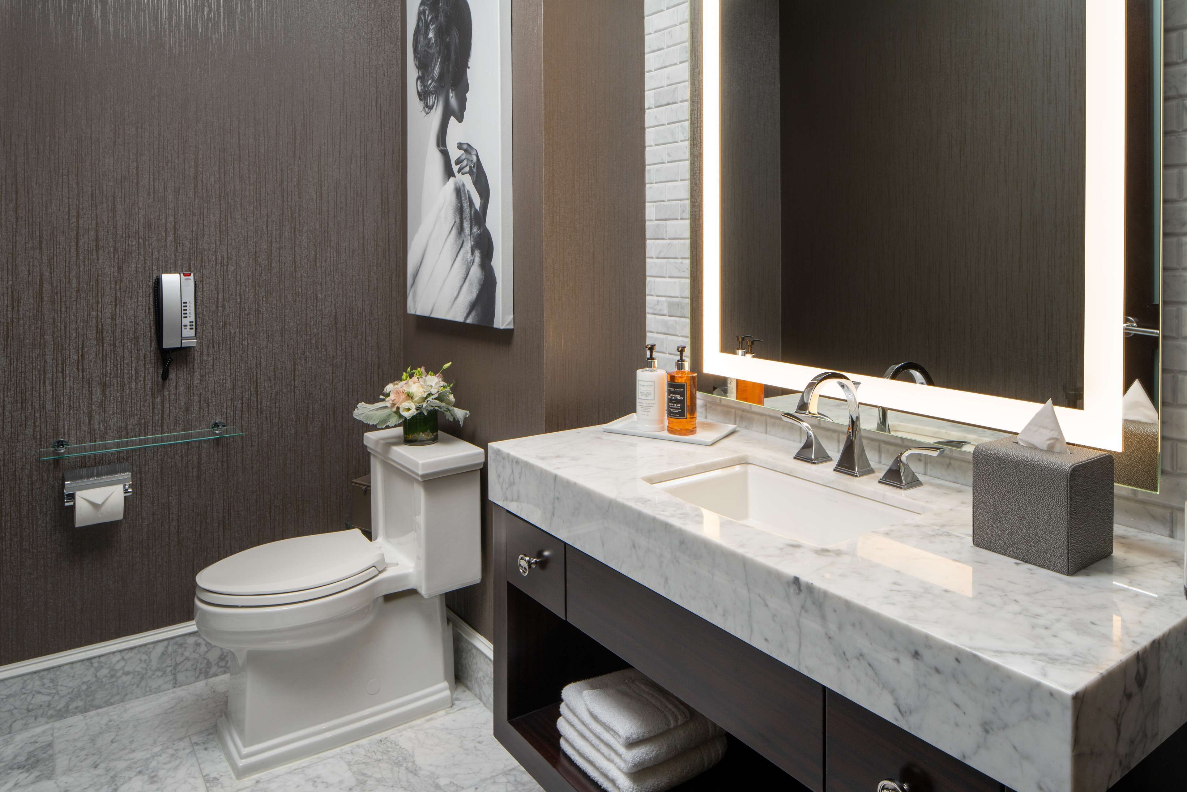 A modern bathroom with a toilet, marble sink, and a large mirror.