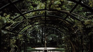 A circular stone table with a central sculpture in a garden under a metal archway. - Châteauhotel en restaurant De Havixhorst (De Schiphorst)