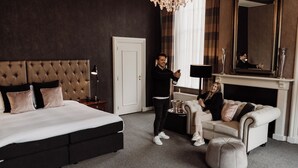 A modern bedroom with a large bed, a white sofa, and a fireplace. - Châteauhotel en restaurant De Havixhorst (De Schiphorst)