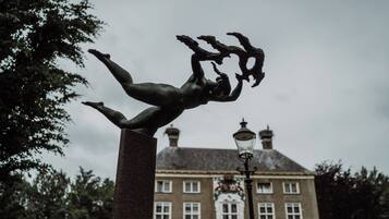 A statue of a human figure in a dynamic pose, set against a backdrop of a historic building with multiple windows and a traditional lamp post.