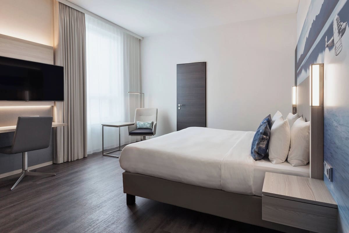Une chambre d’hôtel moderne équipée d’un grand lit, d’un bureau, d’une chaise et d’un téléviseur  à écran plat.