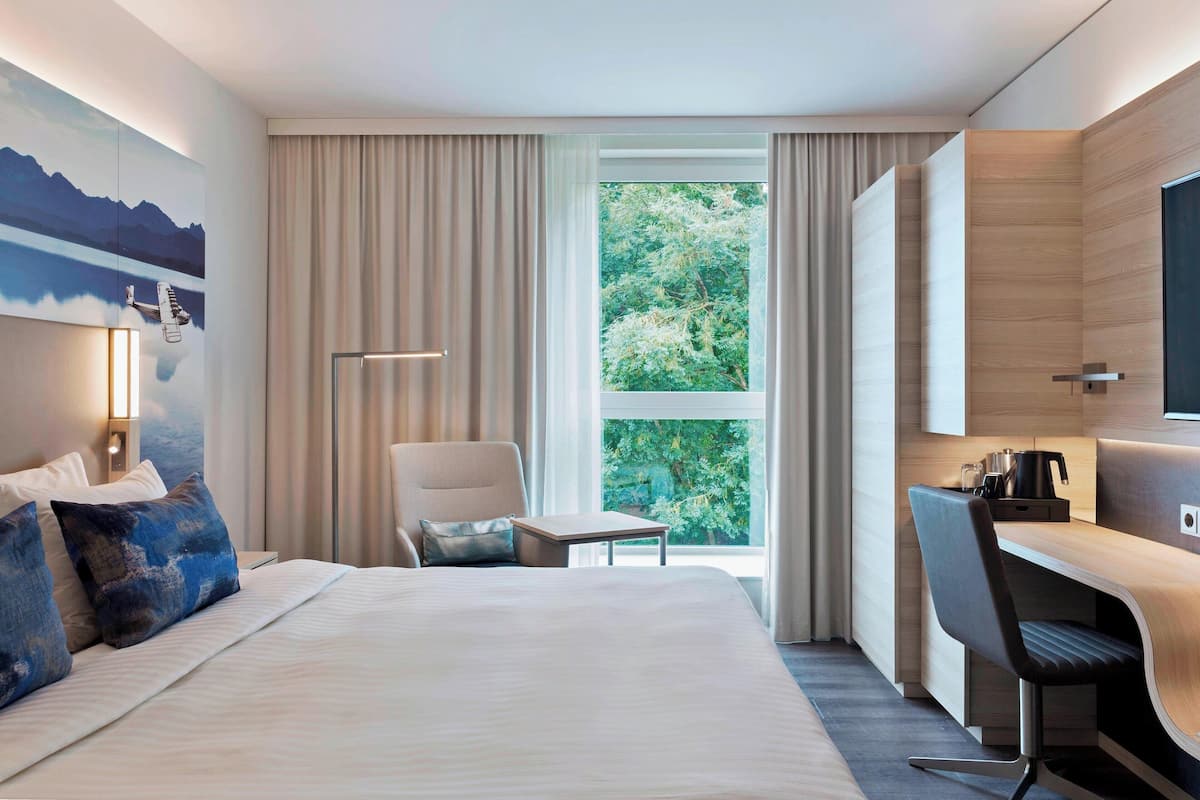 Une chambre d’hôtel équipée d’un lit, d’un bureau, d’une chaise, d’une fenêtre avec des rideaux et d’un téléviseur fixé au mur.