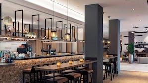 Zona de bar moderna con taburetes, una barra con botellas e iluminación colgante.
