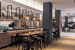 Uma área de bar moderna com banquetas, um balcão com garrafas e iluminação pendente.