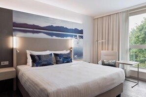 Ett modernt hotellrum med en stor säng, utsikt över bergen genom ett fönster och ett litet bord vid fönstret.