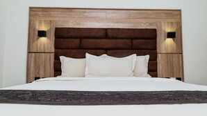 Ein Bett mit hölzernem Kopfteil, zwei Wandleuchten und einer dunkel gemusterten Tagesdecke.