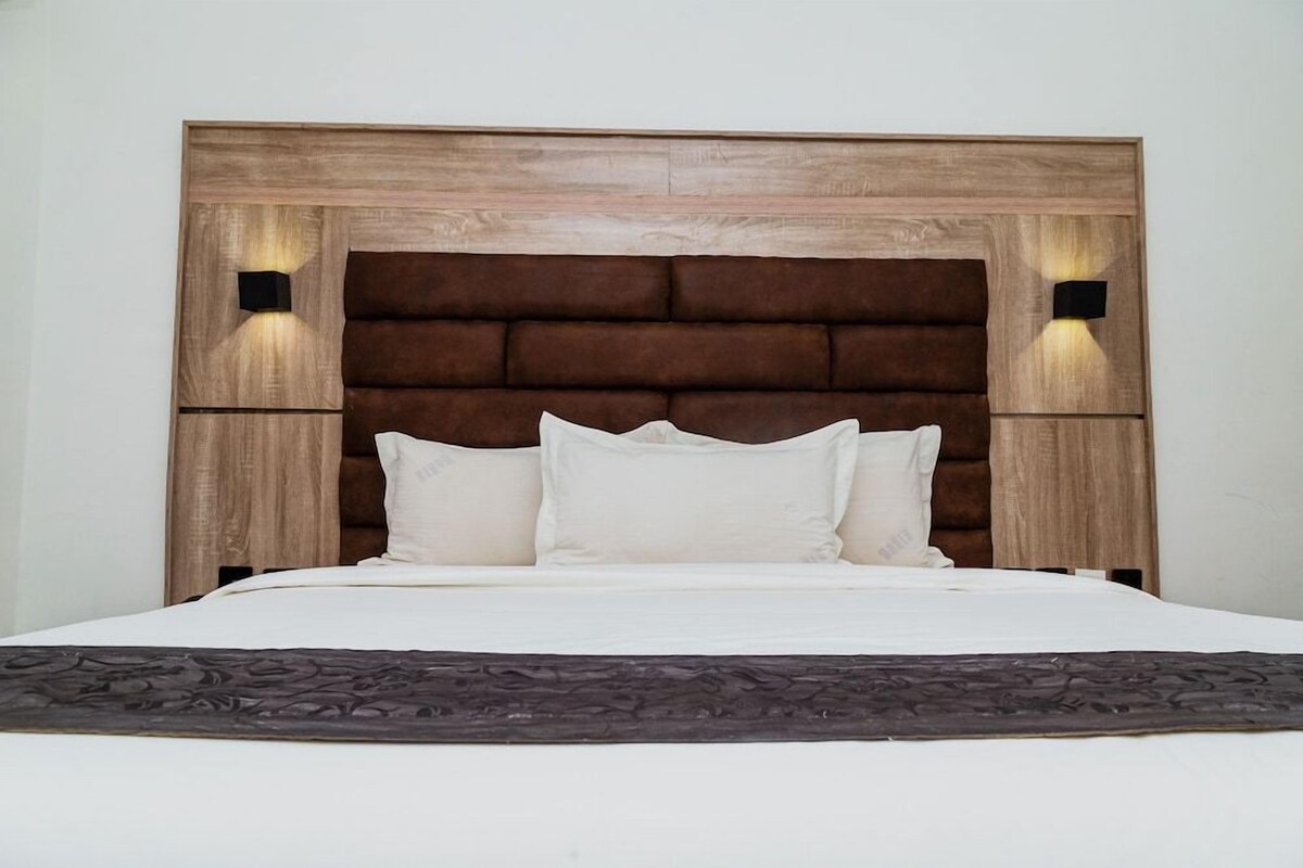 Ein Bett mit Holz-Kopfteil, zwei Wandleuchten und einer dunkel gemusterten Tagesdecke.