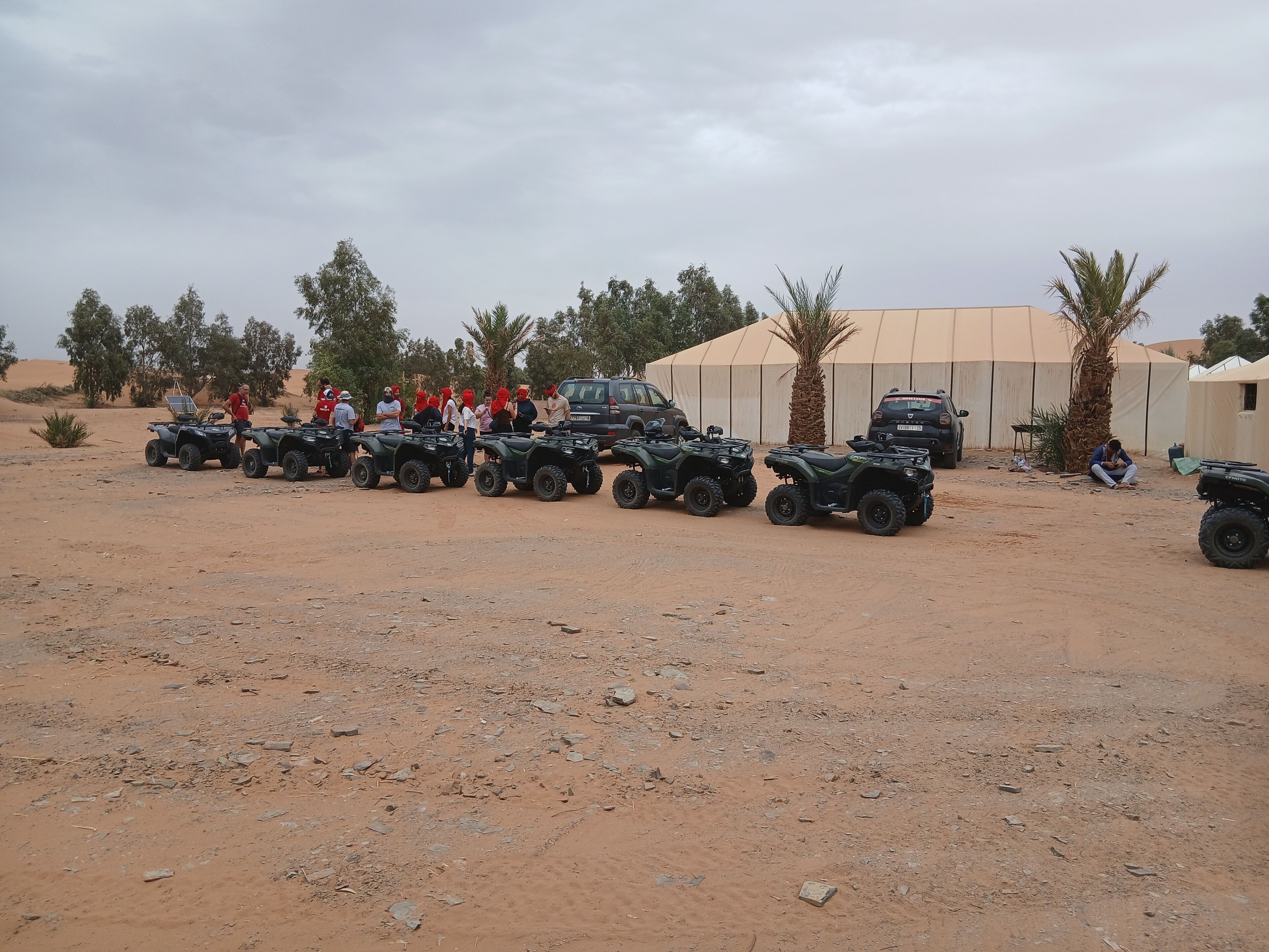 A desert setting with ATVs lined up and a tent structure in the background.