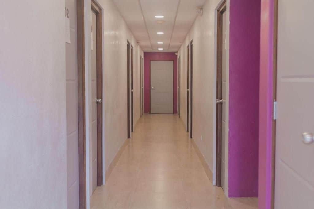 A corridor with doors on both sides, a tiled floor, and a ceiling with recessed lighting.