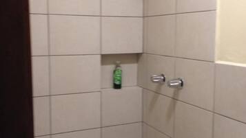 A small, tiled shower stall with a showerhead and a bottle of shampoo on the wall.