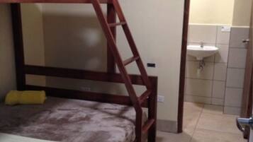 A bunk bed room with a wooden ladder, a single bed with a yellow pillow, and a bathroom with a sink and tiled walls.
