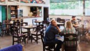 A spacious cafe with high ceilings, exposed beams, and hanging pendant lights. There are several tables and chairs for patrons to sit at. - Airport Inn Managua (Managua)