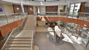 A modern hotel lobby with a central staircase, seating area, and large windows providing views of the outdoors. - NAPA Furnished Suites Square One (Mississauga)
