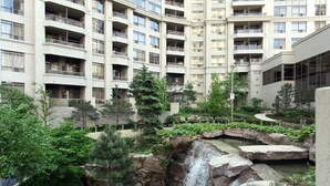 A multi-story residential building with balconies, a landscaped garden with a waterfall, and a stone retaining wall. - NAPA Furnished Suites Square One (Mississauga)