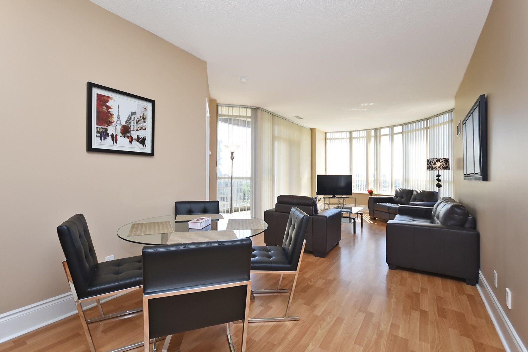 A spacious living room with a glass table, black leather chairs, a sofa, and a flat-screen TV.