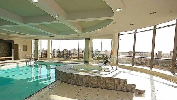 An indoor swimming pool with a view of the city through large windows. - NAPA Furnished Suites Square One (Mississauga)