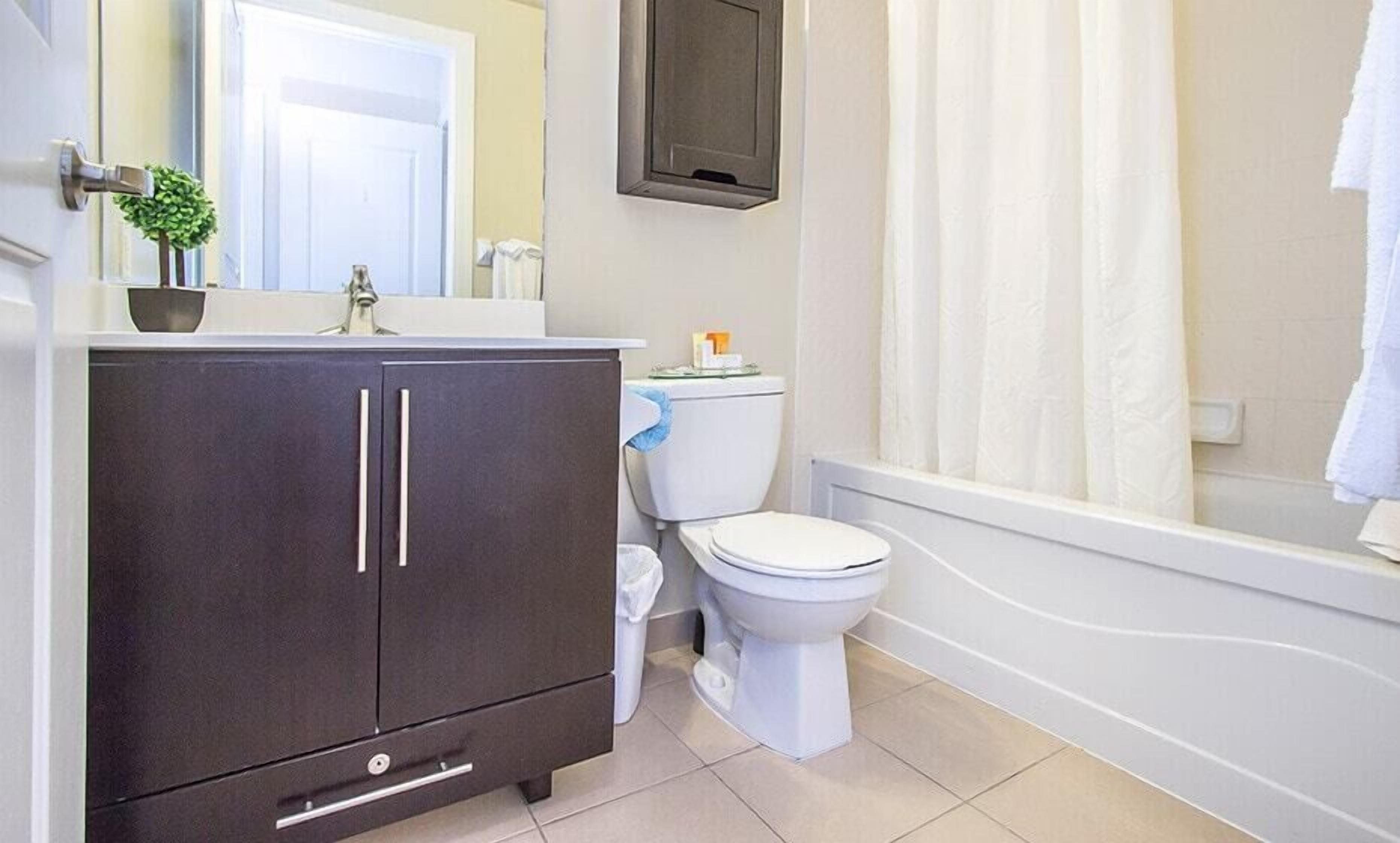 A bathroom with a dark cabinet, a toilet, a bathtub, and a shower curtain.