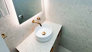 Un baño con lavamanos blanco, espejo y toallero en la pared.