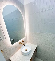 Un baño con lavamanos blanco, espejo y toallero en la pared.