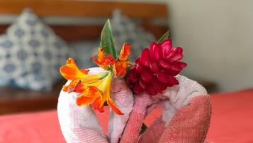 A hand holding a bouquet of flowers, with a patterned pillow and a red bedspread in the background.