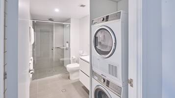 A modern bathroom with a glass shower enclosure, a toilet, and stacked laundry machines.