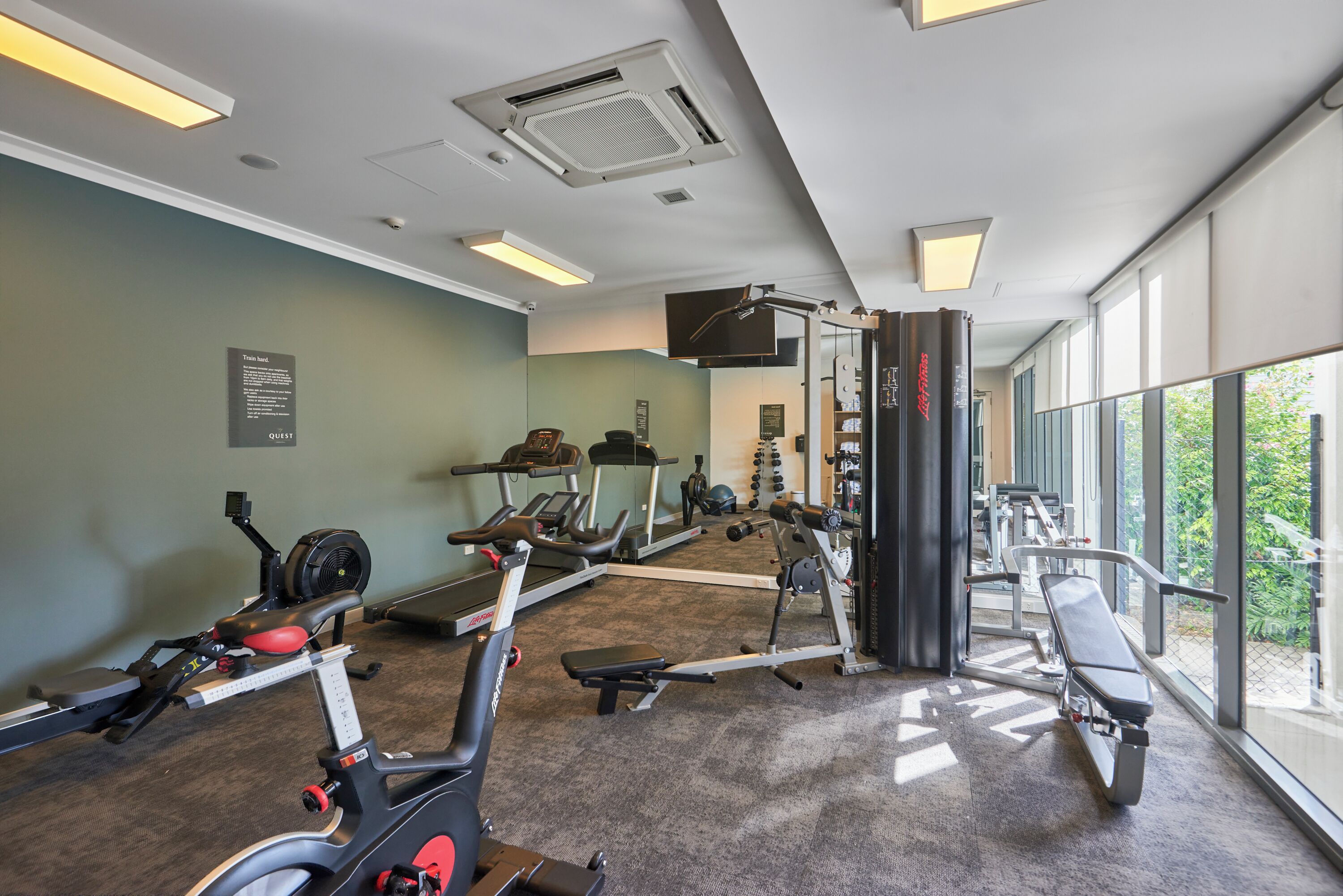 Ginásio com máquinas de cardio, equipamentos de musculação e um espelho grande.