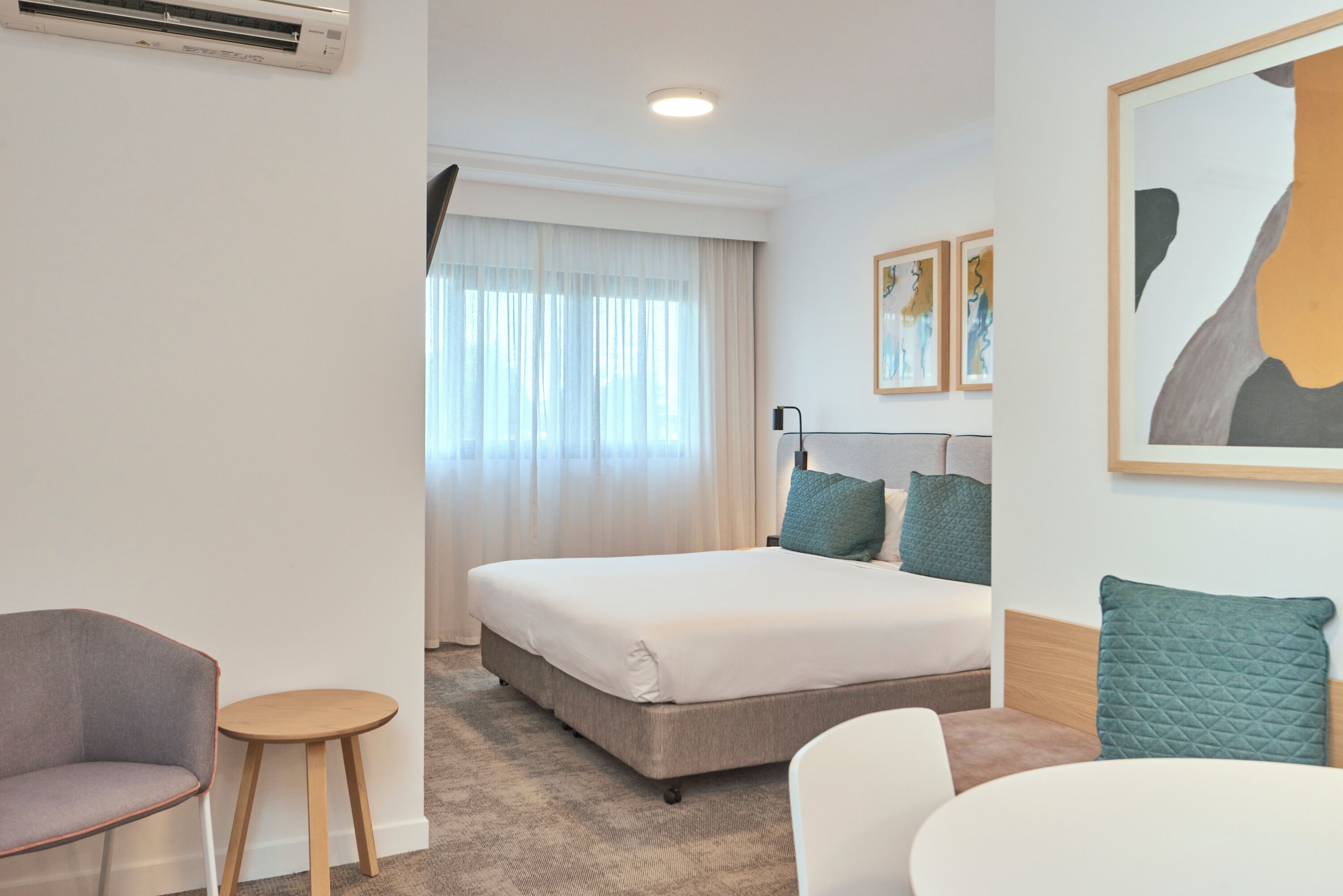 Una habitación de hotel con una cama, una silla, una mesita y un cuadro en la pared.