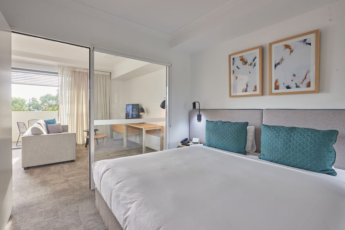 Quarto de hotel com cama, escrivaninha, cadeira e televisão.