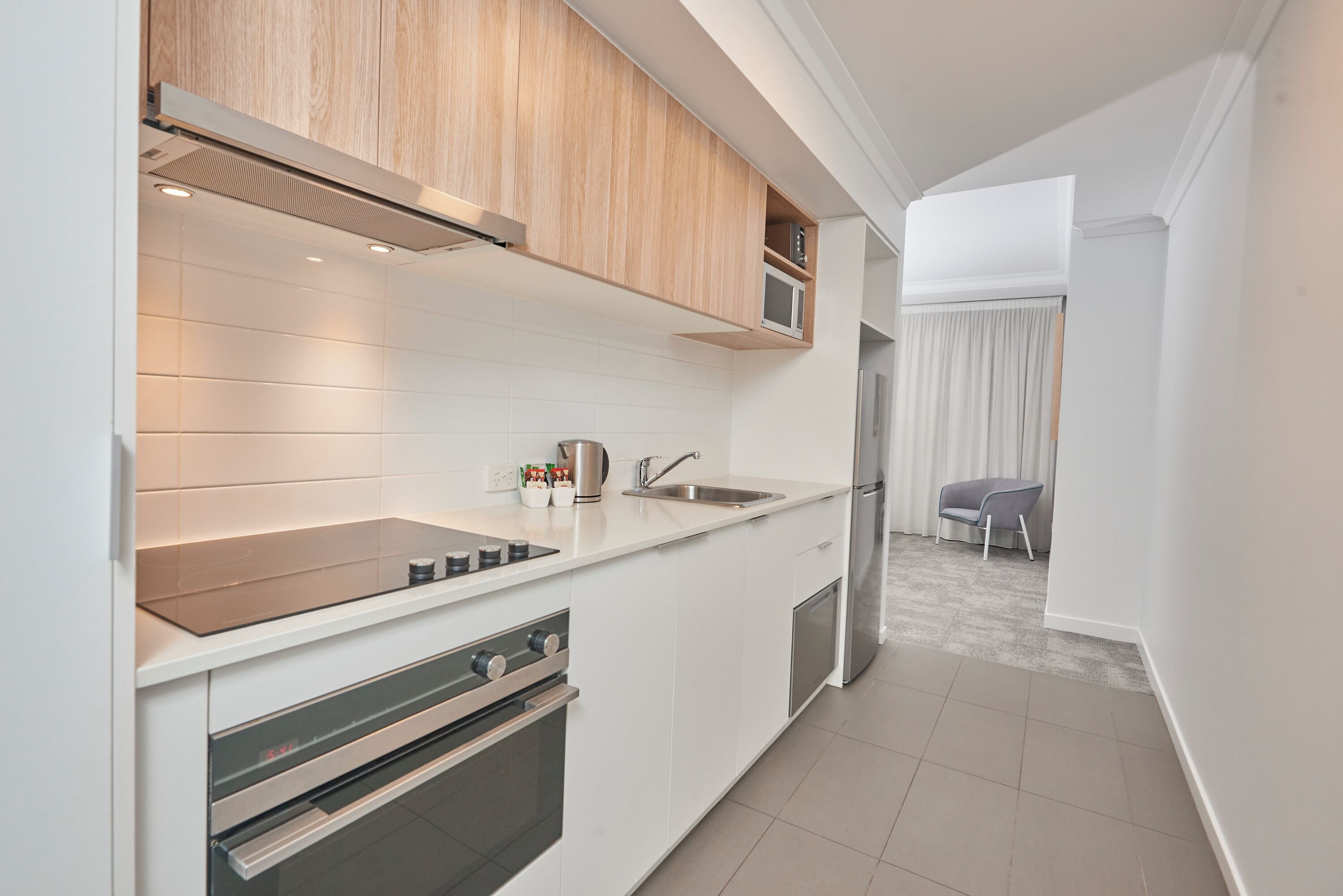 A modern kitchen with white cabinetry, a built-in microwave, stainless steel appliances, and a small dining area with a chair.