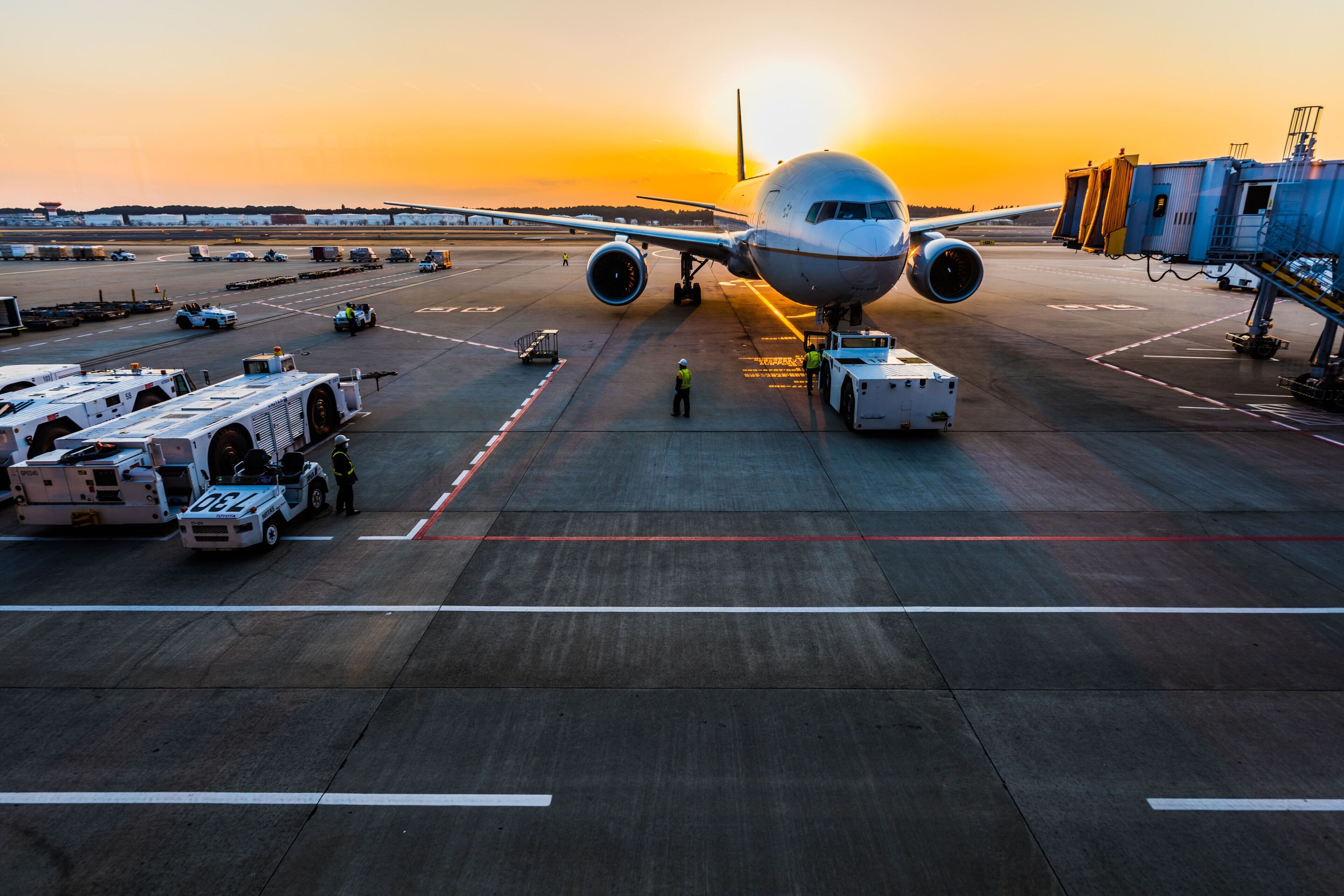 An airport tarmac with an airplane parked, ground crew, and airport service vehicles.