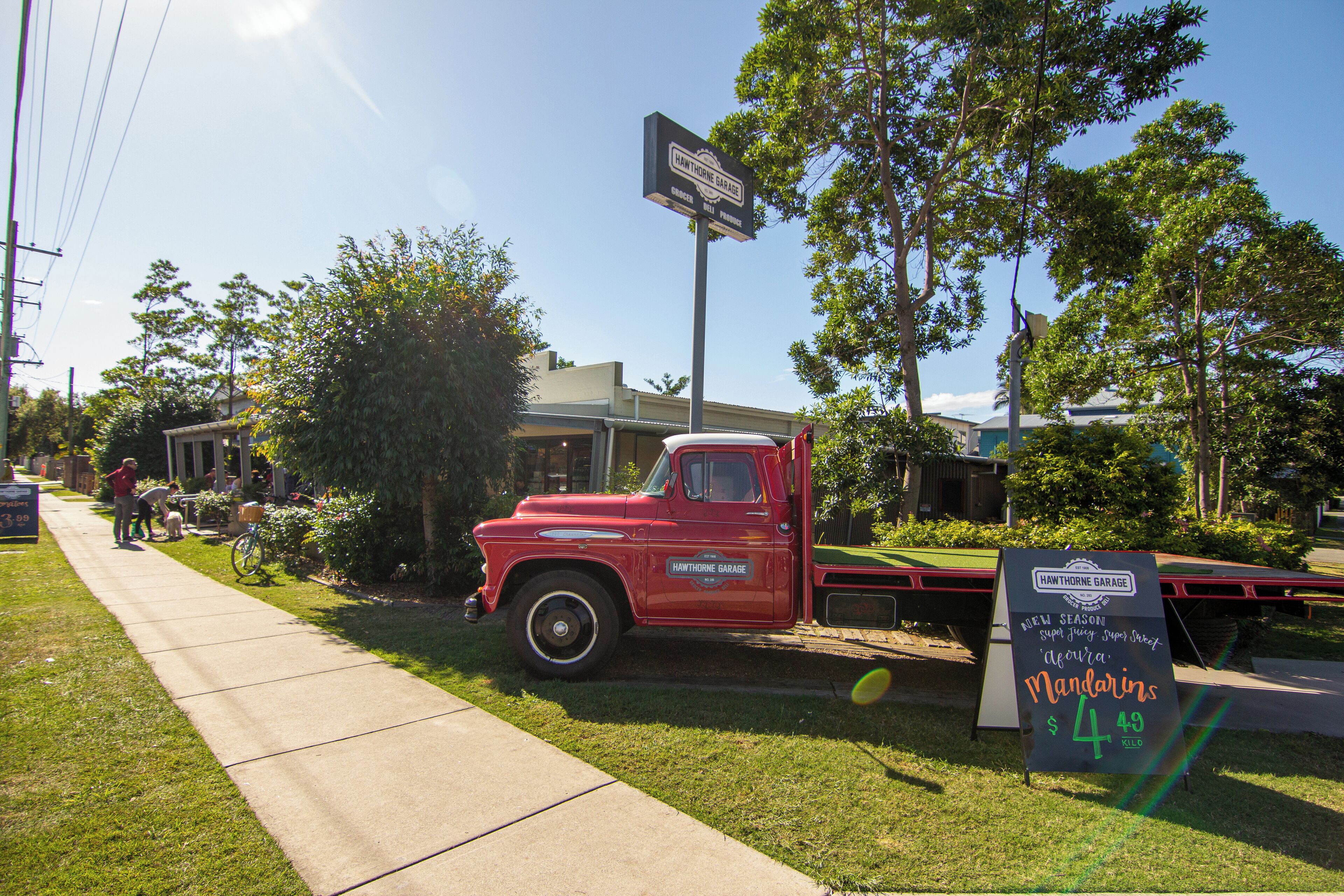 A red vintage truck parked on a grassy area with a signboard advertising 'Hawthorne Garage' and 'Mandarins' for $4.49.