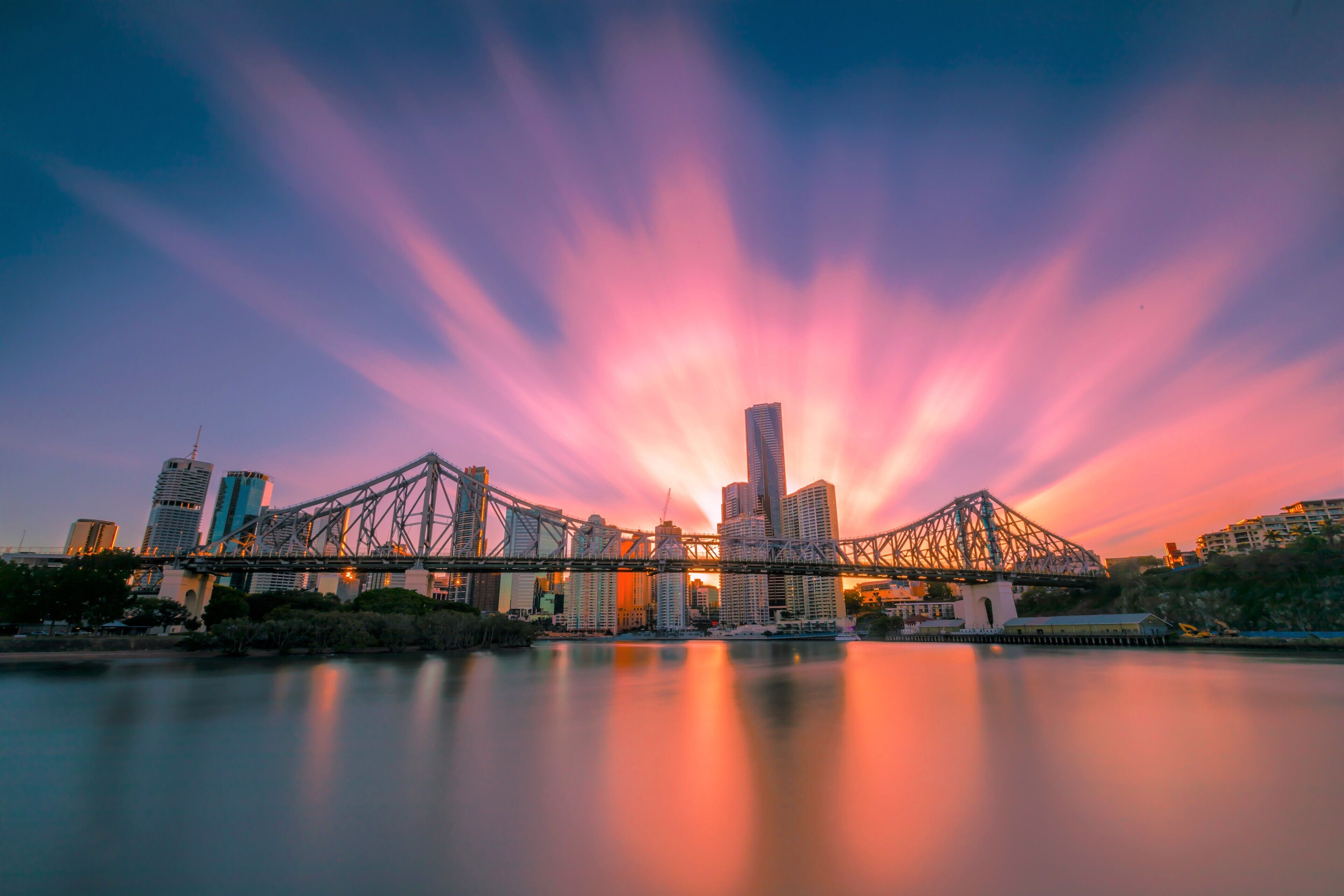 A city skyline with a prominent bridge and skyscrapers during sunset.