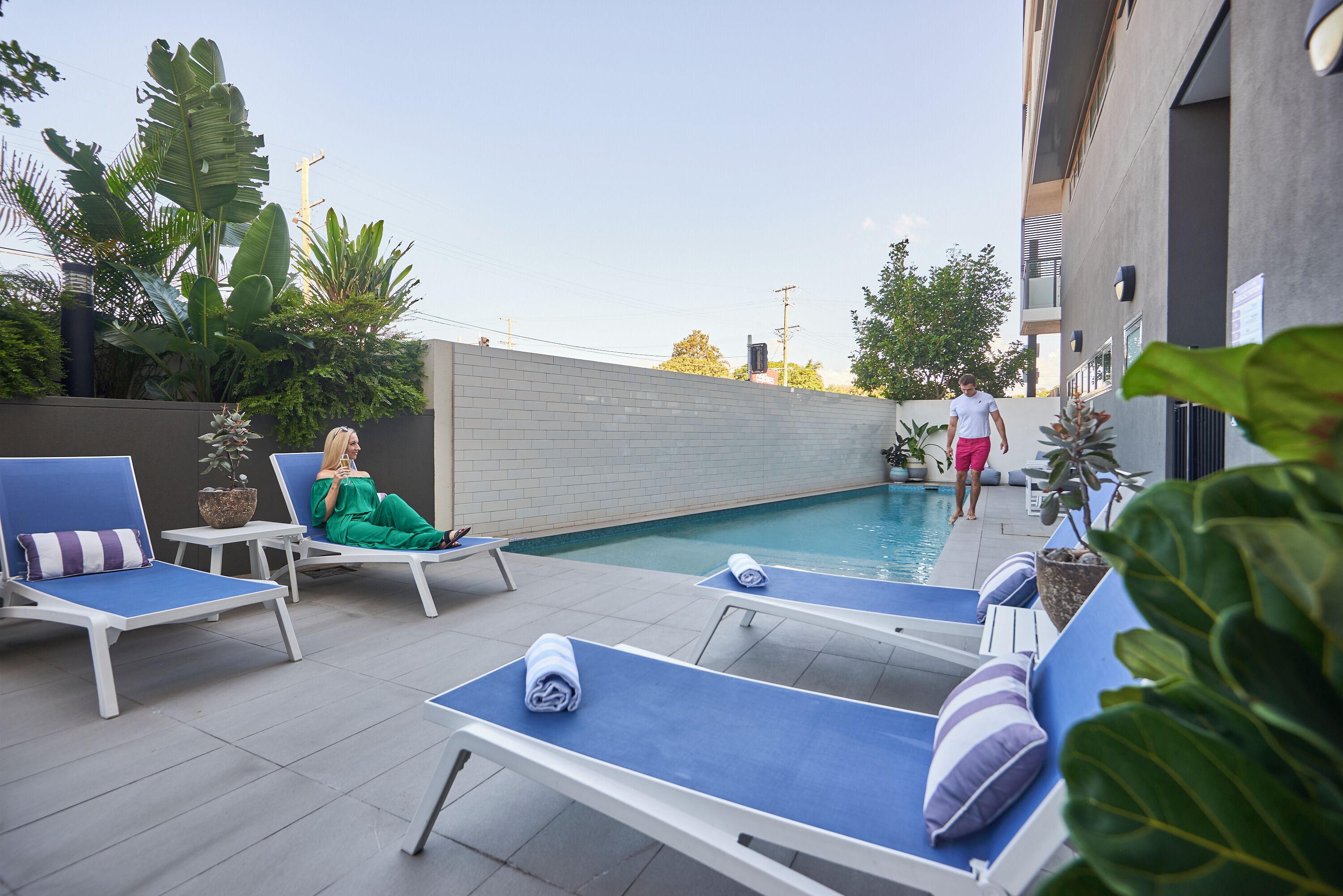 A poolside area with lounge chairs, a person in green, and another in pink shorts.
